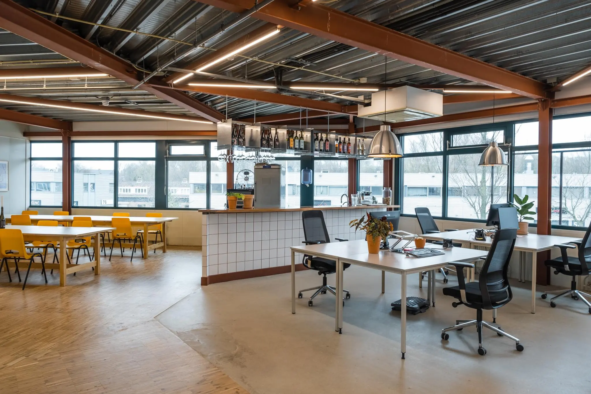 Modern ingerichte kantoorruimte aan de Johan van Hasseltweg met werkplekken, een bar en een zitgedeelte met gele stoelen.